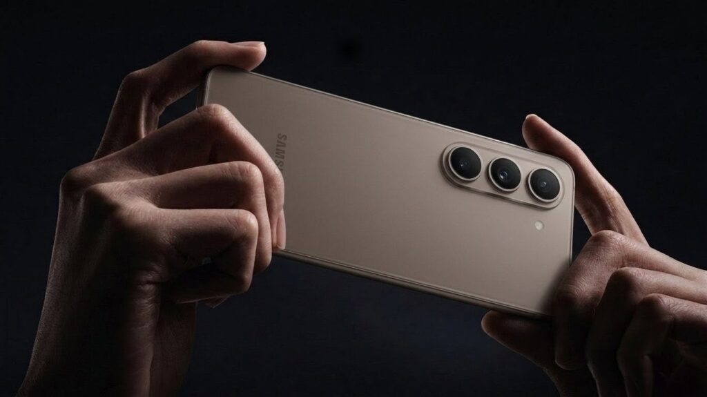 Close-up shot of hands horizontally holding the metallic brown Galaxy S27 concept smartphone, highlighting the triple rear camera lenses and Samsung branding against a dark background.